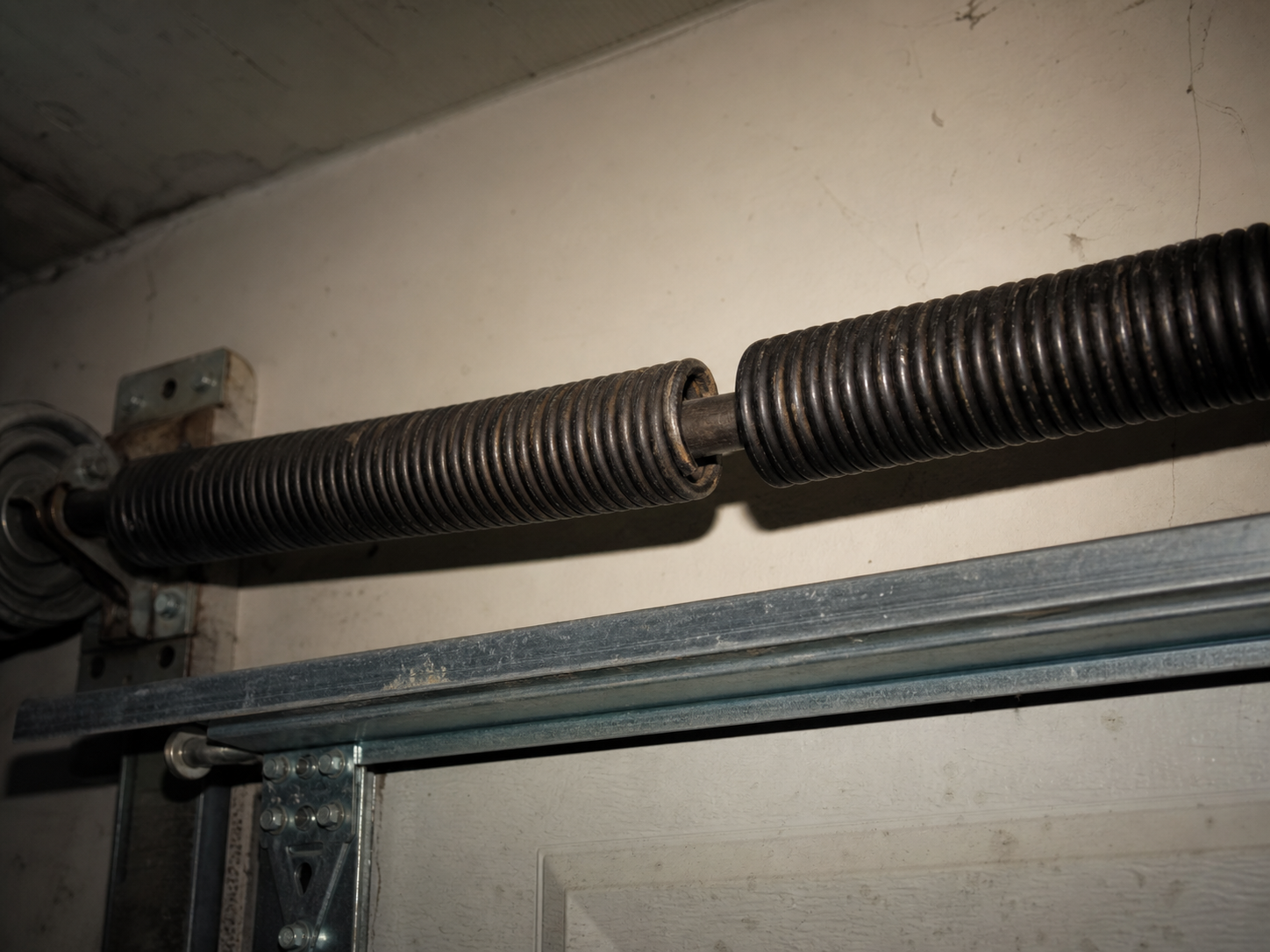 A broken torsion spring on the spring bar above a garage door, showing a clean gap in the coil where it snapped