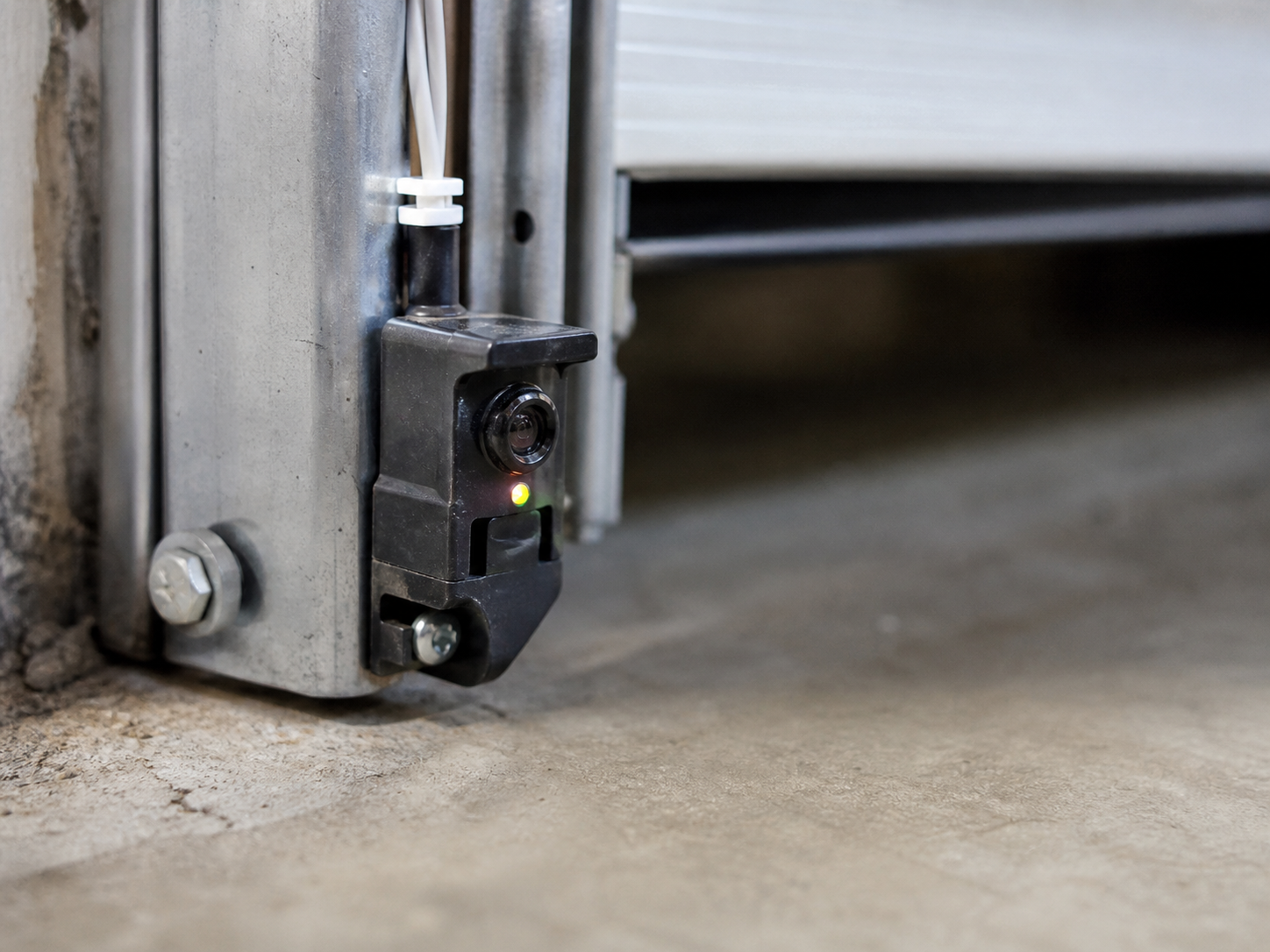 Close-up of a garage door safety photo eye sensor mounted low on the track with its indicator light