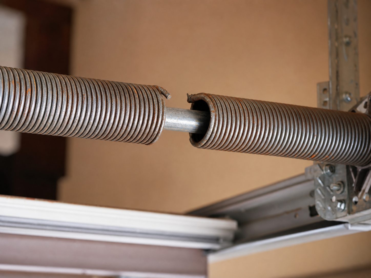 Close-up of a snapped garage door torsion spring on the steel shaft above the door, showing a clear gap where the coil separated
